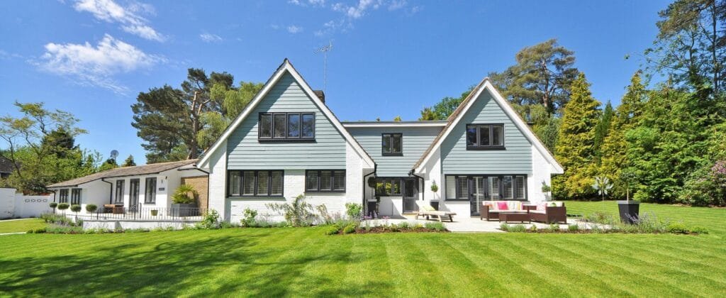 Modern family home exterior showcasing a large lawn and garden under a clear blue sky.