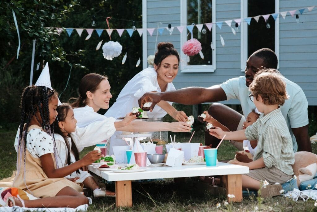 A lively backyard picnic with diverse family and friends sharing food outdoors on a sunny day.