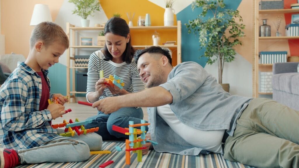 Family building with colorful toy blocks together on floor.